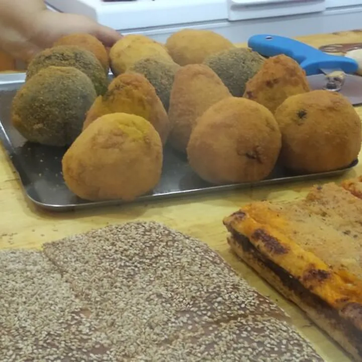 Arancine appena fritte su una teglia, alcune impanate chiare e altre con il pangrattato agli spinaci.