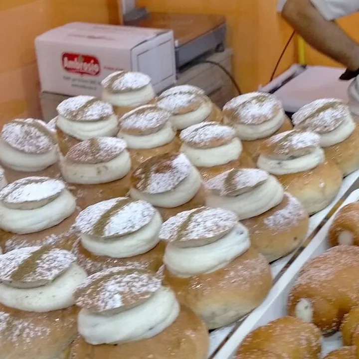 Brioche farcite di crema e spolverate di zucchero a velo, in fila su un vassoio.