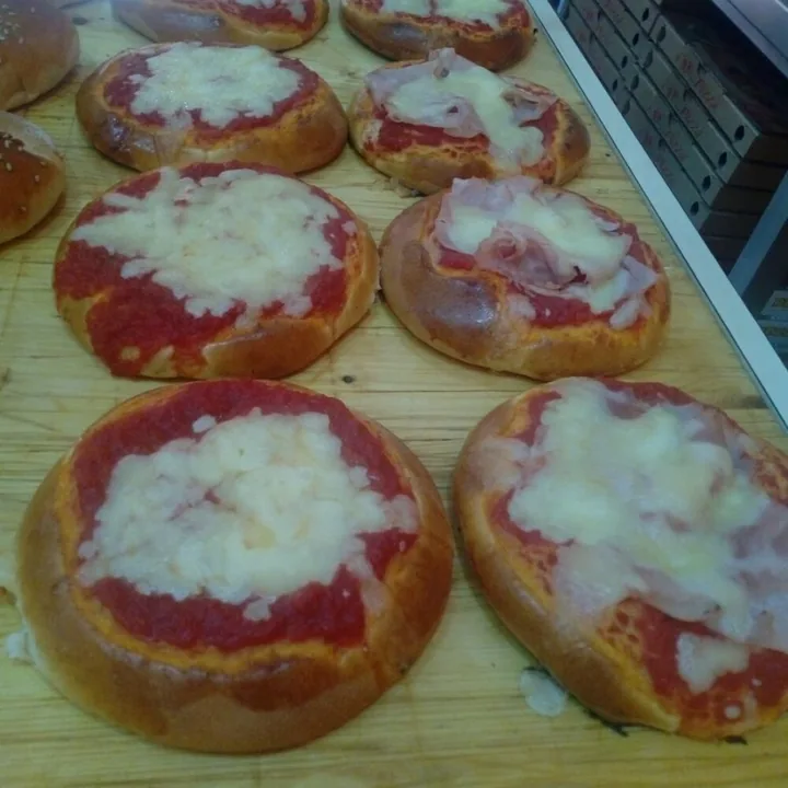 Pizzette palermitane allineate su un piano di legno, con pomodoro e formaggio filante.
